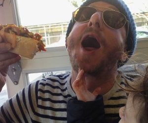 Kid-friendly summer eats in Brooklyn: guy in hat holding loaded hot dog up as toddler reaches for it